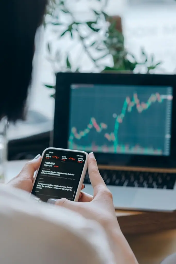 Person using smartphone for stock market analysis at home office.